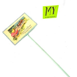 May include: A vintage Easter-themed cake topper featuring a pastel illustration of a chick in a carriage pulled by horses. The topper has a light green stick and a decorative border. The text on the topper reads "Joyous Easter Memories with Greetings Sincere."