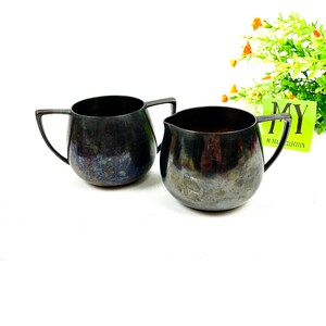 May include: A set of two vintage silver creamer and sugar bowls. The bowls are both round and have a dark, aged finish.