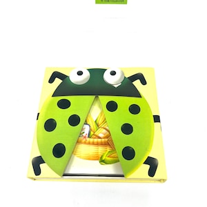 May include: A yellow and green ladybug-shaped book with a white background. The book has a flap that opens to reveal a picture of a basket of corn. The book has the text "MY 3C YEAR COLLECTION" on the front.