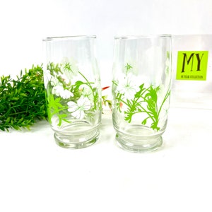 May include: Two clear glass drinking glasses with a green and white floral design. The glasses have a rounded bottom and a straight side.
