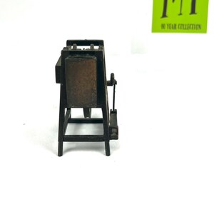 May include: A miniature wooden easel with a brown canvas, a pencil sharpener, and a metal crank. The easel is made of dark brown wood and has a simple design.