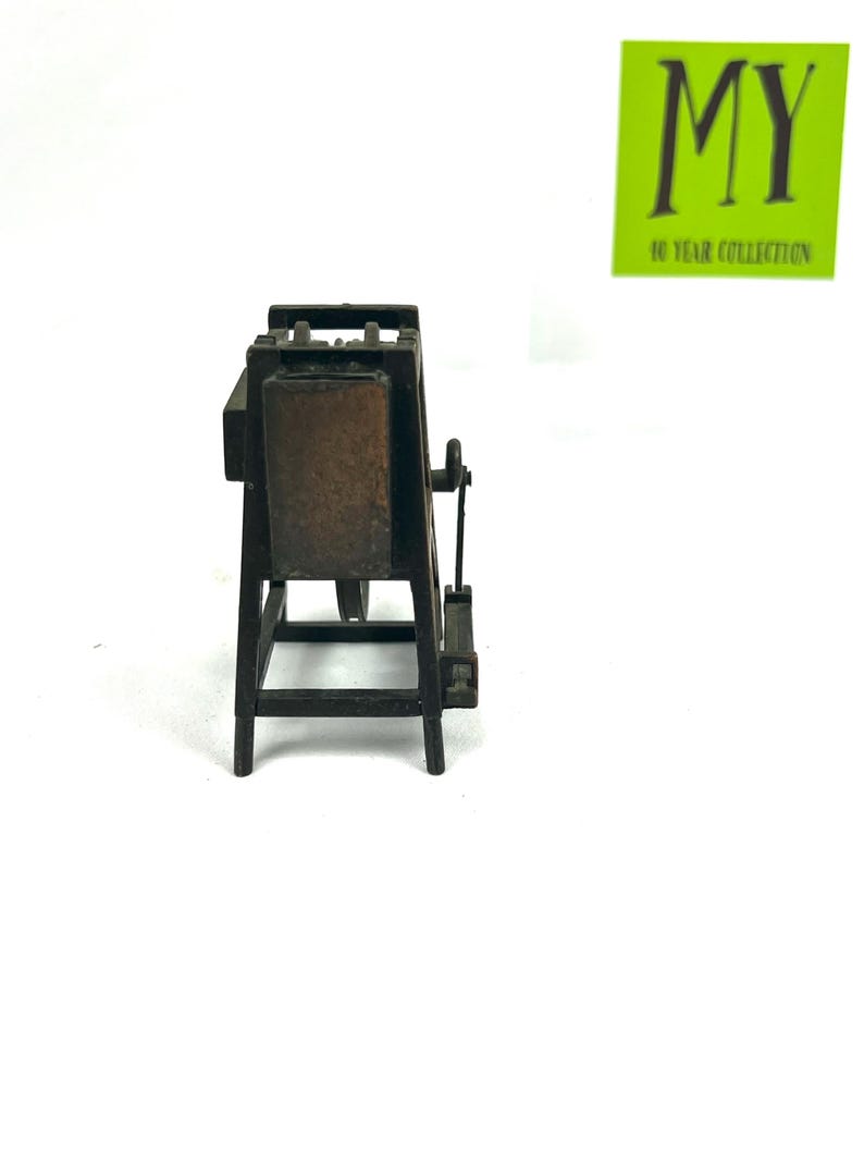 May include: A miniature wooden easel with a brown canvas, a pencil sharpener, and a metal crank. The easel is made of dark brown wood and has a simple design.