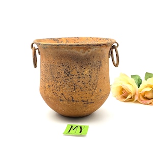 May include: A rusty metal planter with two handles. The planter is brown and has a distressed look.