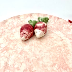 May include: A pink ceramic serving plate with a marbled design. Two small ceramic radishes with green tops are on the plate.