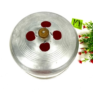 May include: Silver cake cover with a round, ridged top and four red painted apples. The cover has a small, round, wooden knob in the center.