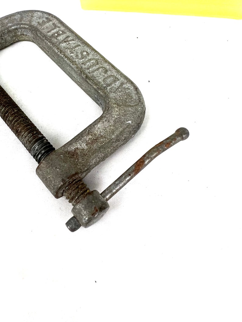 May include: A silver metal C-clamp with a threaded screw and a handle. The clamp is labeled "JAWISCO".