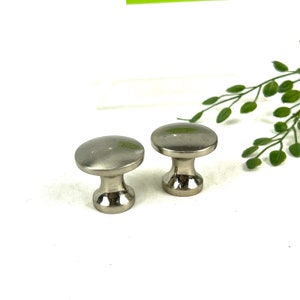 May include: Two silver metal cabinet knobs with a round top and a cylindrical base.