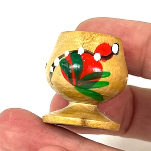 Peut inclure: Une petite tasse en bois avec un motif floral peint. La tasse est peinte avec des fleurs rouges, vertes et blanches. La tasse a une base ronde.