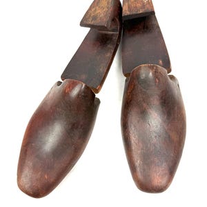 May include: Two wooden shoe trees, designed to maintain the shape of shoes. The shoe trees are a dark brown color, with a smooth, polished finish. The heel section is a lighter brown. The shoe trees are positioned against a white background.