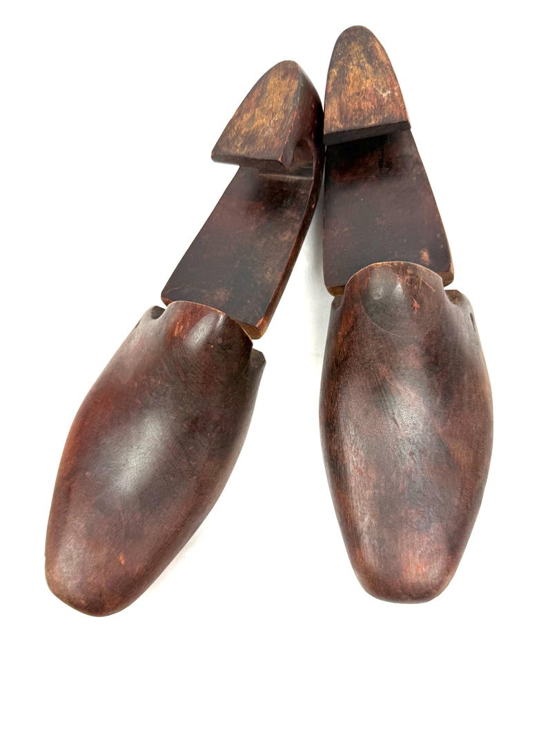 May include: Two wooden shoe trees, designed to maintain the shape of shoes. The shoe trees are a dark brown color, with a smooth, polished finish. The heel section is a lighter brown. The shoe trees are positioned against a white background.