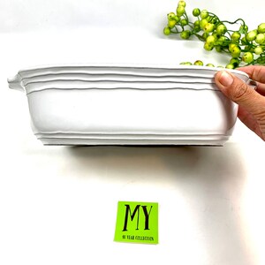 Peut inclure: Un pot rectangulaire en céramique blanche avec un bord légèrement surélevé et un design texturé. Le pot est présenté de côté et a une base noire.