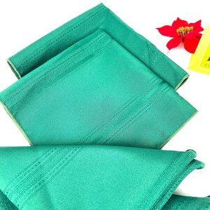 May include: Three green linen napkins with a subtle striped pattern. The napkins are folded and stacked on top of each other.