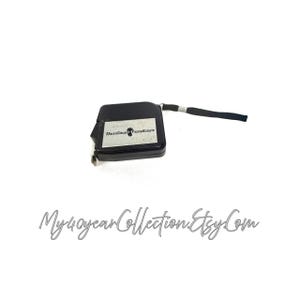 May include: A black measuring tape with a silver accent and a black wrist strap. The tape measure has a silver label with text. The text "My40yearCollection.Etsy.Com" is written in cursive at the bottom of the image.