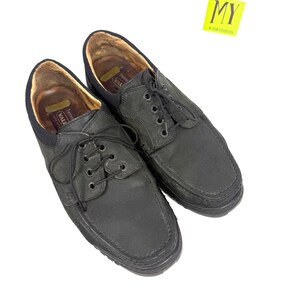 May include: A pair of black leather shoes with a lace-up design. The shoes have a rounded toe and a thick sole. The interior of the shoes is a light brown color. The shoes are displayed on a white background. A yellow sticker with the letters "MY" is in the upper right corner.