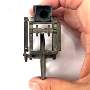 May include: A vintage metal pencil sharpener with a black plastic top and a metal crank. The sharpener has a metal frame and a metal wheel.