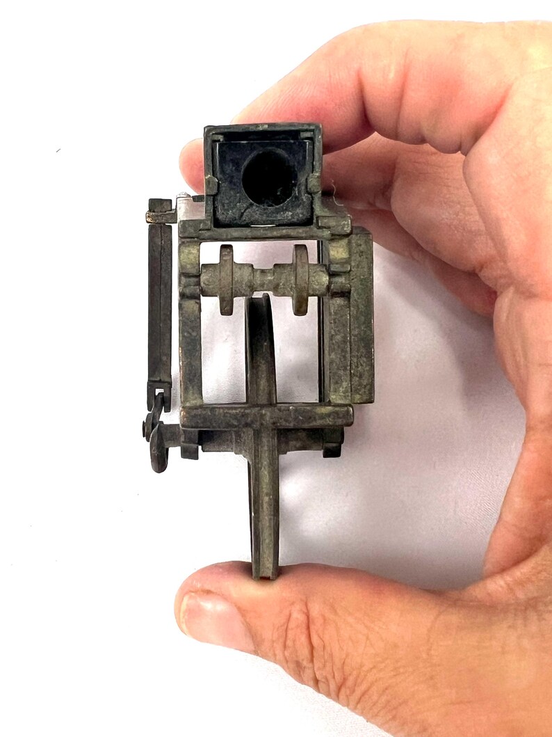 May include: A vintage metal pencil sharpener with a black plastic top and a metal crank. The sharpener has a metal frame and a metal wheel.