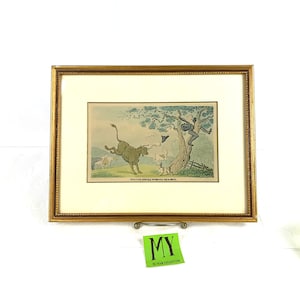 Peut inclure: Impression encadrée dans un cadre doré. L'impression représente un taureau chargeant, une personne grimpant à un arbre et d'autres animaux. Le texte en bas indique "Doctor Royal's Pursuing the Bull."