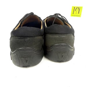 May include: Pair of black leather shoes with laces. The shoes have a rounded toe and a thick, textured sole. The heel area is a darker shade of black. The shoes are displayed against a white background.