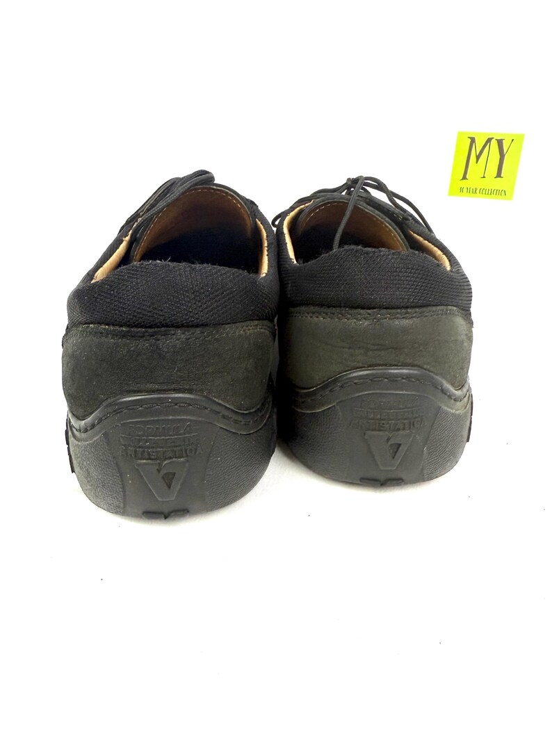 May include: Pair of black leather shoes with laces. The shoes have a rounded toe and a thick, textured sole. The heel area is a darker shade of black. The shoes are displayed against a white background.
