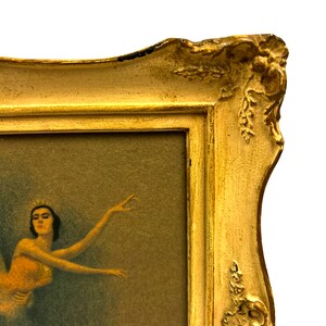 May include: A gold-toned ornate frame with a ballerina painting inside. The ballerina is wearing a white tutu and a crown. The background is a muted green.