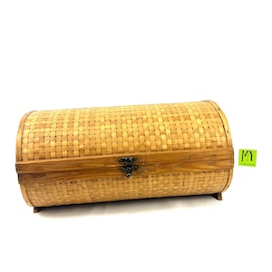 May include: A cylindrical woven wicker storage box with a wooden lid and a metal latch. The box is made of natural brown wicker and has a light wood finish.