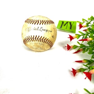 May include: A vintage baseball with the words "Official League" printed on it. The ball is white with red stitching and has a worn, aged appearance.
