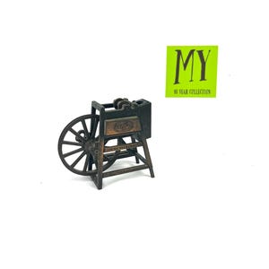 May include: A vintage-style metal pencil sharpener shaped like a small wooden wheel with a crank. The sharpener is brown and black and has the word "Playtime" on the side.