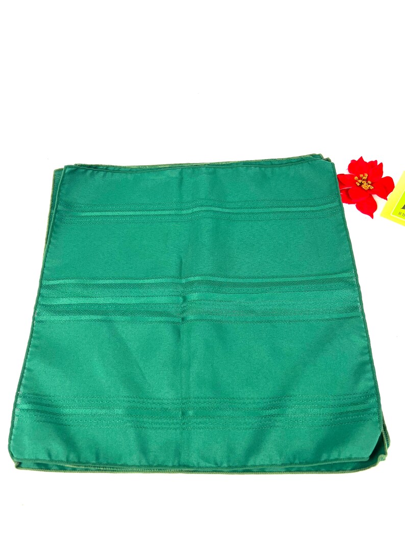 May include: A stack of four green dinner napkins with a subtle striped pattern. The napkins are folded in half and have a smooth, silky texture.