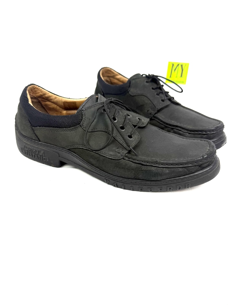 May include: A pair of black leather shoes with laces. The shoes have a rounded toe and a thick sole. The interior is a light brown color. A yellow tag is attached to one shoe. The shoes are displayed on a white background.