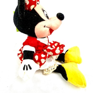 May include: A plush Minnie Mouse doll, featuring a red dress with white polka dots, a matching bow, and yellow shoes. The doll has black fur, white gloves, and a smiling expression. A classic Disney character.