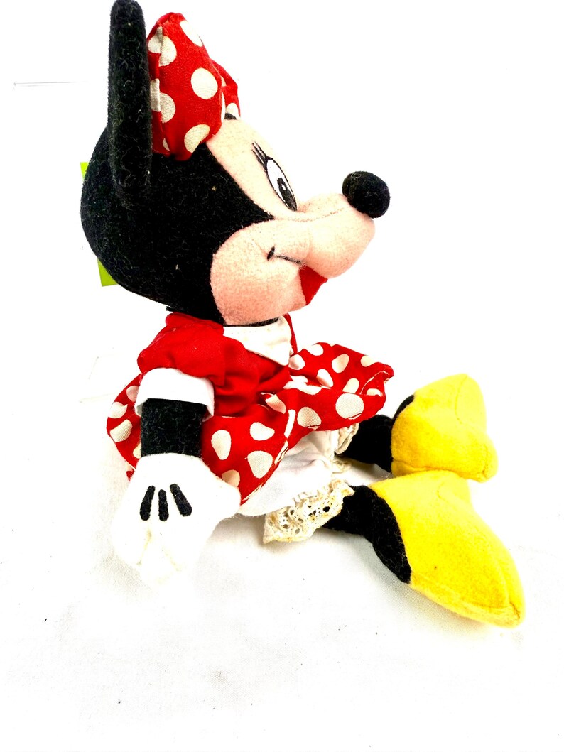 May include: A plush Minnie Mouse doll, featuring a red dress with white polka dots, a matching bow, and yellow shoes. The doll has black fur, white gloves, and a smiling expression. A classic Disney character.