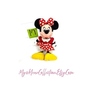 Vintage Minnie Mouse plush doll wearing a red polka dot dress and bow, displayed upright on a white background.