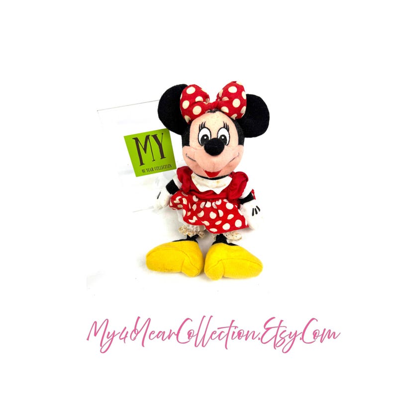 Vintage Minnie Mouse plush doll wearing a red polka dot dress and bow, displayed upright on a white background.