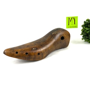 May include: A vintage wooden shoe last with multiple holes. The last is brown and has a smooth, worn surface.