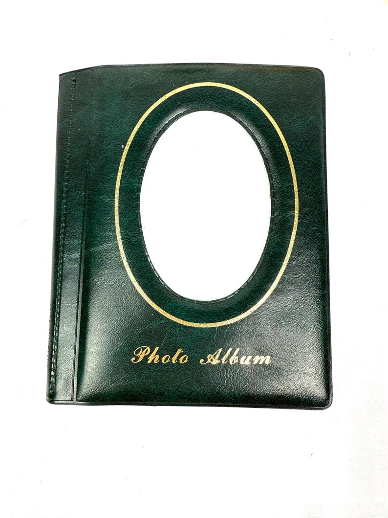 Peut inclure: Un album photo vert fonc&eacute; avec un cadre ovale dor&eacute; et l'inscription "Photo Album" en lettres dor&eacute;es. L'album a une texture lisse semblable &agrave; du cuir et un design classique.
