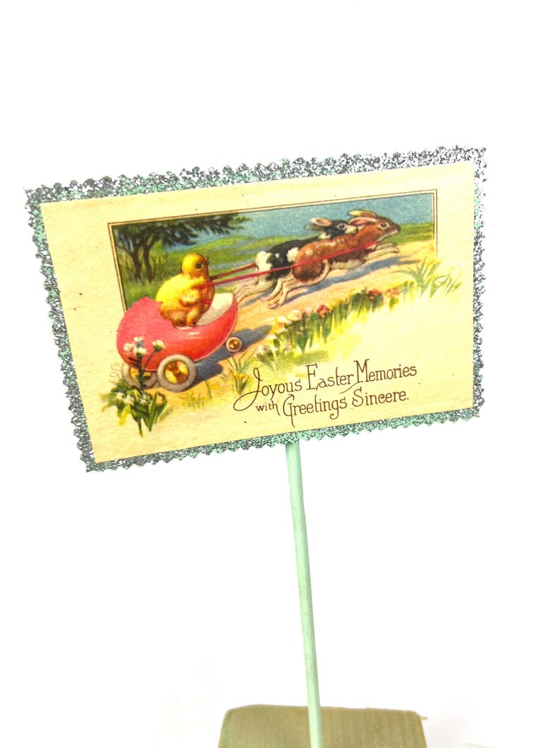 May include: Vintage Easter greeting card featuring a yellow chick in a red wagon pulled by two rabbits. The card has a decorative silver glitter border and text that reads "Joyous Easter Memories with Greetings Sincere."