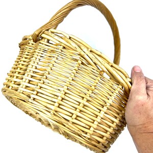 May include: A woven wicker basket with a natural brown color and a single handle. The basket is empty and appears to be made of natural materials.