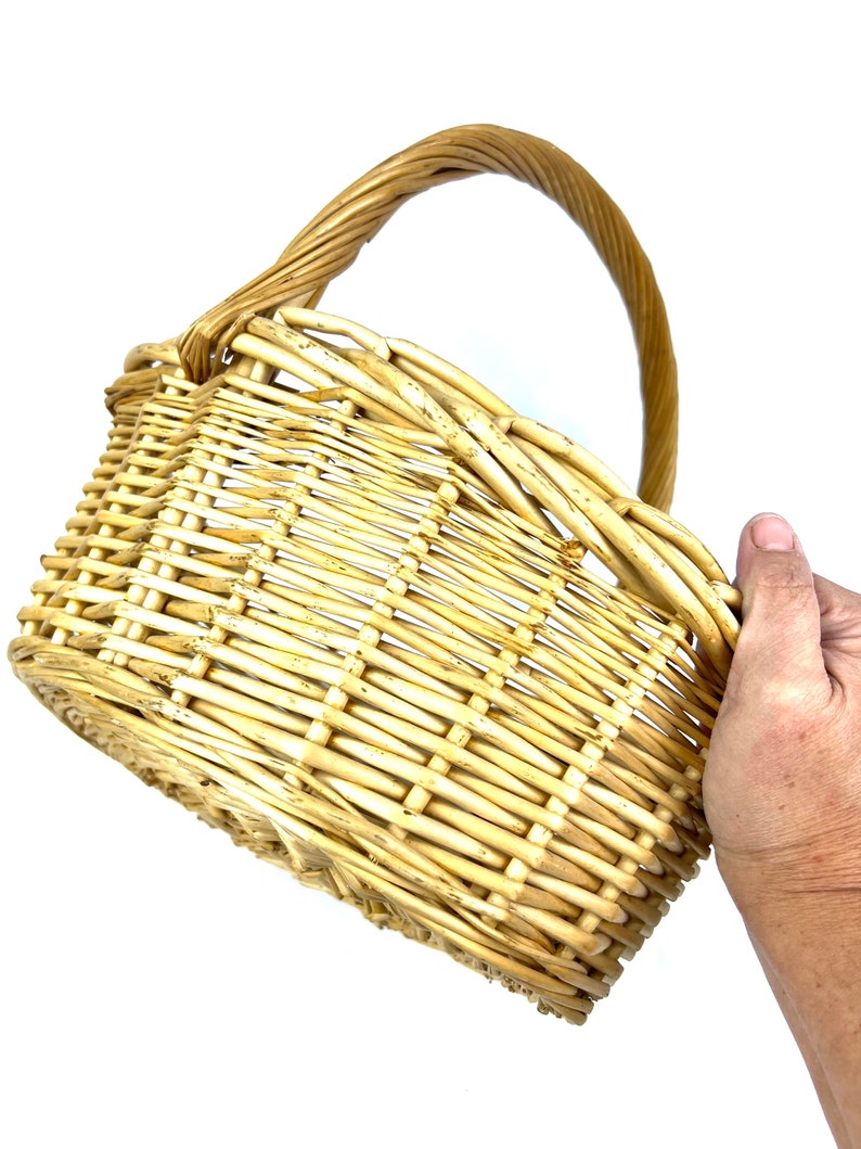 May include: A woven wicker basket with a natural brown color and a single handle. The basket is empty and appears to be made of natural materials.