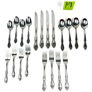 May include: A collection of ornate silverware, including spoons, knives, and forks, arranged on a white surface. The silverware has a detailed floral pattern on the handles. The image includes a logo in the upper right corner.