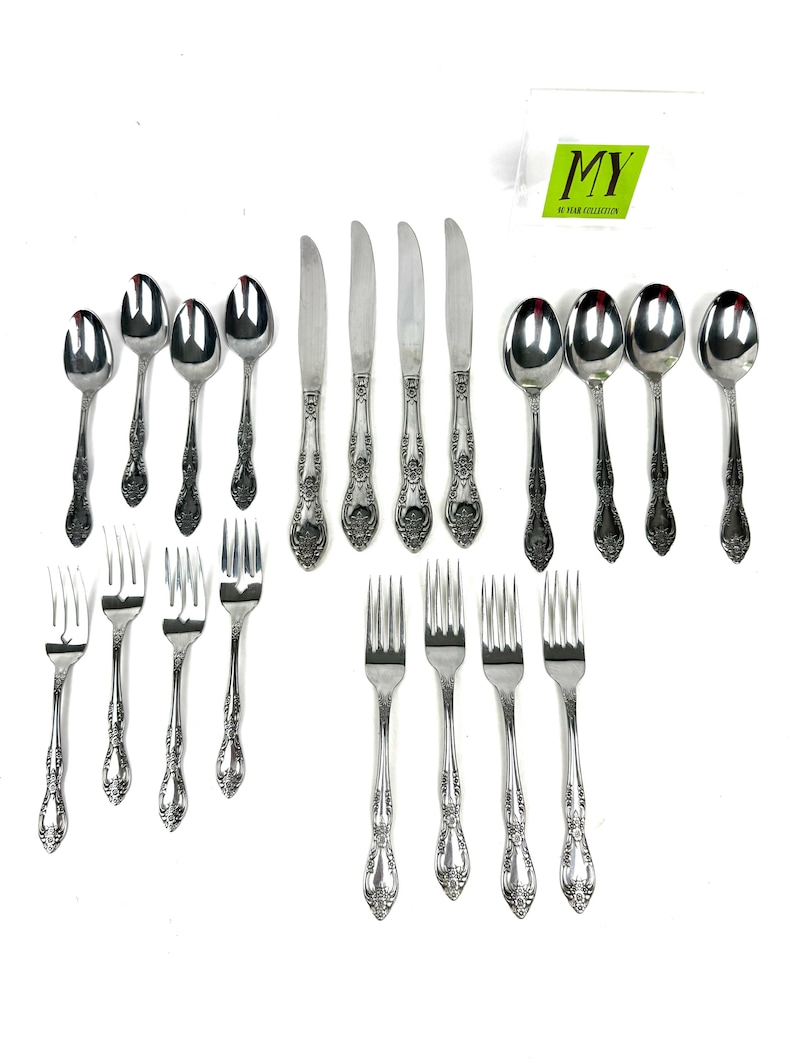 May include: A collection of ornate silverware, including spoons, knives, and forks, arranged on a white surface. The silverware has a detailed floral pattern on the handles. The image includes a logo in the upper right corner.