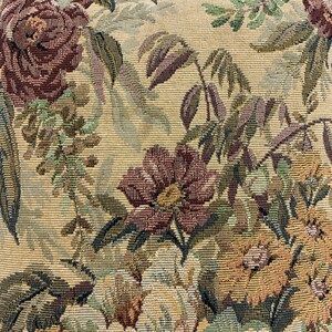 May include: A close-up of a beige fabric with a floral tapestry pattern. The fabric features a variety of flowers, including roses and other blooms in shades of brown, green, and yellow.