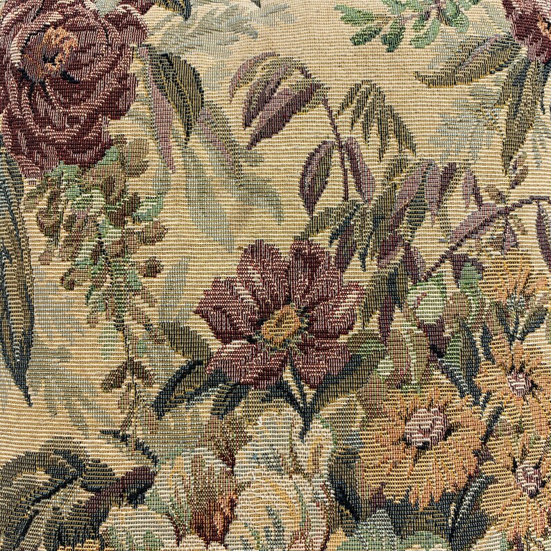 May include: A close-up of a beige fabric with a floral tapestry pattern. The fabric features a variety of flowers, including roses and other blooms in shades of brown, green, and yellow.