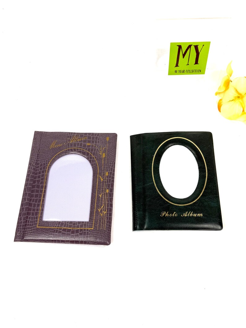 Peut inclure: Deux albums photo. L'un est marron fonc&eacute; avec une fen&ecirc;tre rectangulaire et des accents dor&eacute;s. L'autre est vert fonc&eacute; avec une fen&ecirc;tre ovale et une bordure dor&eacute;e. Les mots "Photo Album" sont imprim&eacute;s sur le devant.