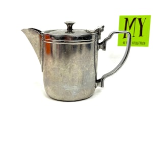 May include: A vintage silver-toned creamer with a lid and handle. The creamer has a spout for pouring and a small knob on the lid. The handle is curved and attached to the side of the creamer. The text "MY 10 Y COLLECTION" is on a green sticker.