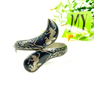 May include: A silver bangle bracelet with black enamel and intricate silver filigree designs. The bracelet features two figures of dancers in silver.