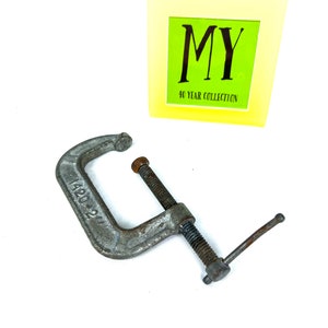 May include: A silver metal C-clamp with a threaded screw and a handle. The clamp is marked with the number "1420-21".