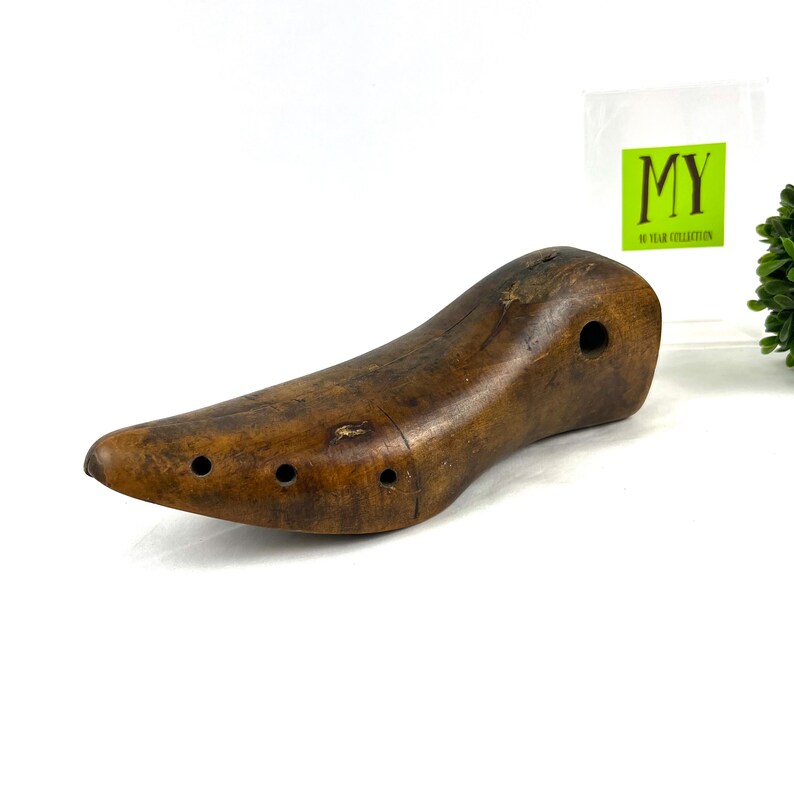 May include: A brown wooden shoe stretcher with multiple holes. The stretcher is shaped like a shoe and is designed to help maintain the shape of shoes.
