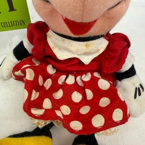 May include: A vintage Minnie Mouse plush doll. The doll features a red dress with white polka dots, a white collar, and black and white striped sleeves. The doll has yellow shoes and white gloves. The doll's face is pink with a red smile.