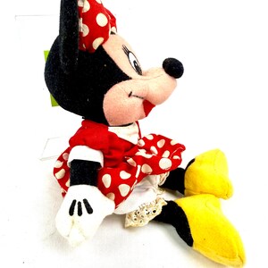 May include: A plush Minnie Mouse doll, featuring a red dress with white polka dots and a matching bow. The doll has black ears, a pink face, white gloves, and yellow shoes. The doll is a classic Disney character.