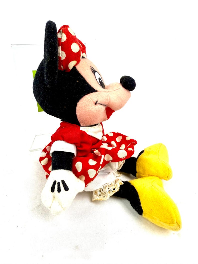 May include: A plush Minnie Mouse doll, featuring a red dress with white polka dots and a matching bow. The doll has black ears, a pink face, white gloves, and yellow shoes. The doll is a classic Disney character.